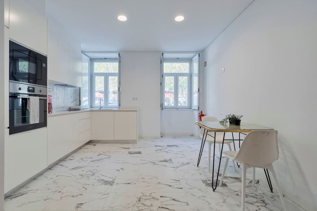 Uma cozinha moderna com armários brancos, forno embutido e uma área de refeições com mesa e cadeiras.
