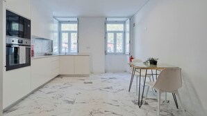 A modern kitchen with white cabinets, a built-in oven, and a dining area with a table and chairs. - Vita Luxus (Setúbal)