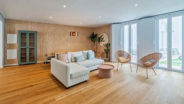 A modern living room with a white sofa, two clear chairs, a round coffee table, and a wooden wall with a herringbone pattern. - Vita Luxus (Setúbal)