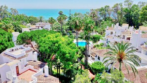A residential area with white buildings, a swimming pool, and a view of the sea.
