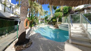 A swimming pool with a thatched roof, palm trees, and a staircase leading to a poolside area.