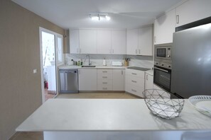 A modern kitchen with white cabinets, a stainless steel refrigerator, and a built-in oven. - 2035 Modern Family Apartment on Golden Beach (Marbella)
