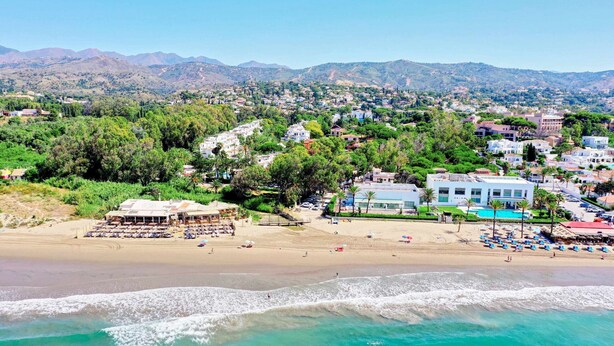 A coastal town with a beach, a pool area, and a view of mountains in the background.