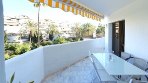 A balcony with a white table and chairs, overlooking a residential area with palm trees and buildings.