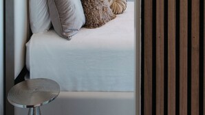A modern bedroom with a bed, pillows, a small side table, and a window. - Lux Coastal Retreat & Hot Tub (Oak Harbor)
