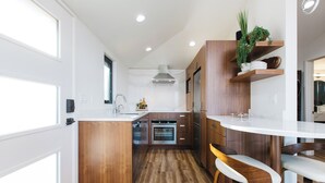A modern kitchen with wooden cabinets, a central island, and a bar area with stools. - Lux Coastal Retreat & Hot Tub (Oak Harbor)
