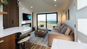 A modern living room with a large window, a sofa, a coffee table, and a TV. - Lux Coastal Retreat & Hot Tub (Oak Harbor)