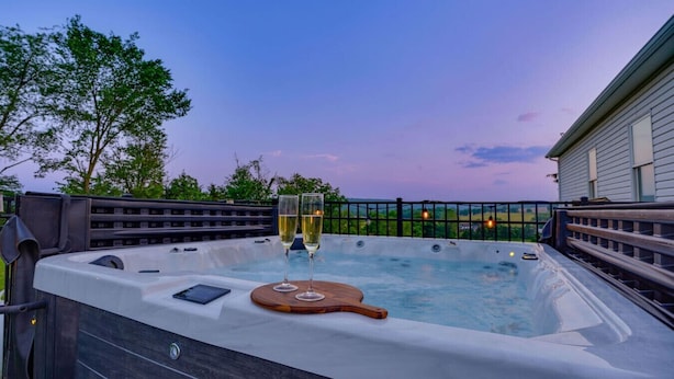 A hot tub with two glasses of champagne, surrounded by a wooden deck and a metal fence. - Willow Brook Mansion, an upscale retreat in the countryside with heated seasonal (May 1st - Oct. 1st) pool, hot tub and game room. (Millerstown)