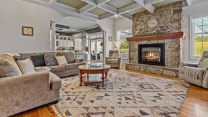 A spacious living room with a stone fireplace, a large sofa, and a coffee table. - Willow Brook Mansion, an upscale retreat in the countryside with heated seasonal (May 1st - Oct. 1st) pool, hot tub and game room. (Millerstown)