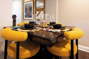 Une table à manger avec quatre chaises, chacune agrémentée d’un coussin jaune, mise avec des verres à vin, des bols et une boîte de mouchoirs.