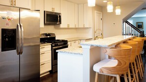 A kitchen with a stainless steel refrigerator, a microwave, a stove, and wooden bar stools. - Spacious Fed Hill Home w/Rooftop & 4 Parking Spots (Baltimore)