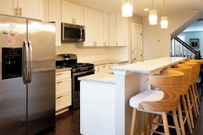 A modern kitchen with stainless steel appliances, a central island with bar stools, and a staircase leading to another level.