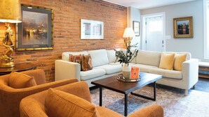 A living room with a brick wall, a white sofa, a coffee table, and a lamp. - Spacious Fed Hill Home w/Rooftop & 4 Parking Spots (Baltimore)
