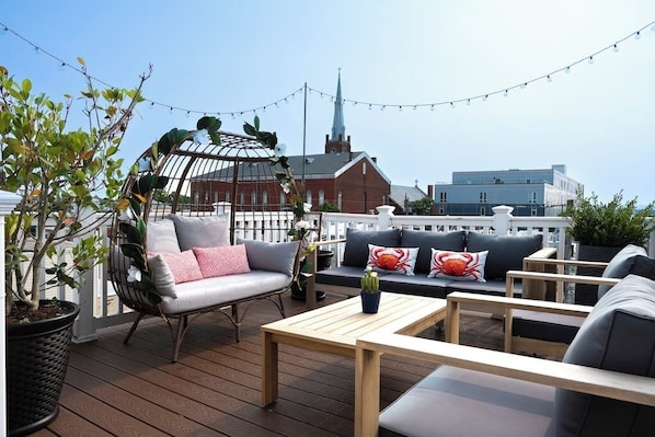 A rooftop deck with outdoor seating, a potted plant, and a view of a church steeple.