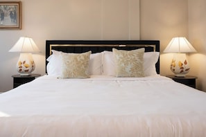 A neatly made bed with white linens and decorative pillows, flanked by two bedside tables with lamps.