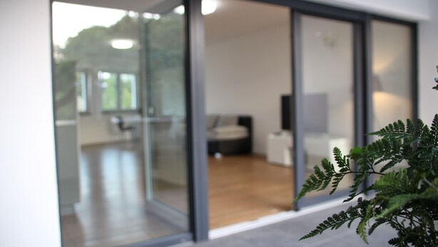 A modern interior with a glass door leading to a spacious room with a bed and a desk. - Top Appartment in Hilden to rent, Lift, Fully furnished with equipped kitchen, (Hilden, Nordrhein-Westfalen, Deutschland)