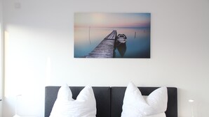 A modern room with a grey sofa, white pillows, a painting of a pier, and a bedside table with a lamp. - Top Appartment in Hilden to rent, Lift, Fully furnished with equipped kitchen, (Hilden, Nordrhein-Westfalen, Deutschland)
