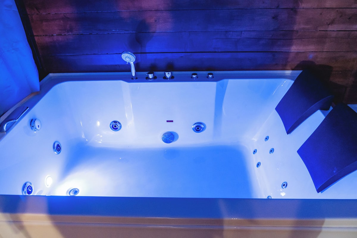 A large, rectangular hot tub with multiple jets, set against a wooden wall.