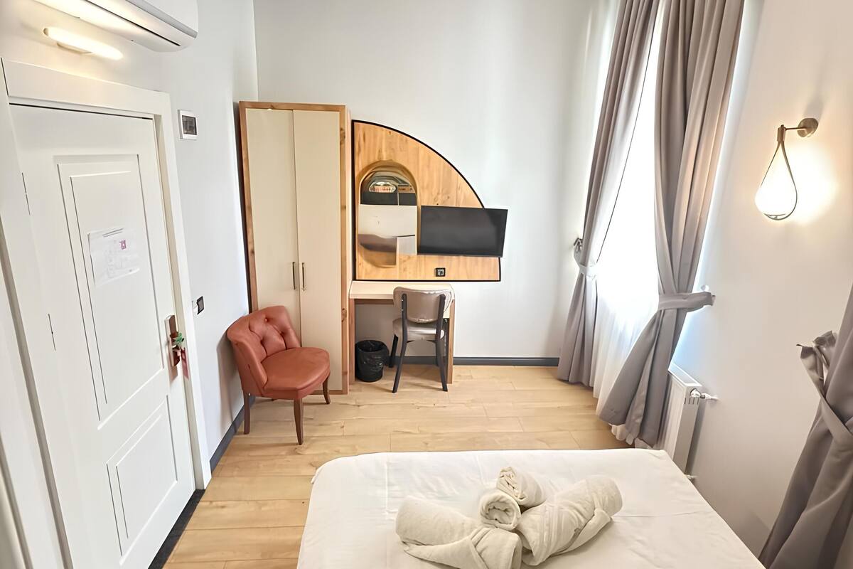 A hotel room with a bed, a desk, a chair, and a wardrobe.