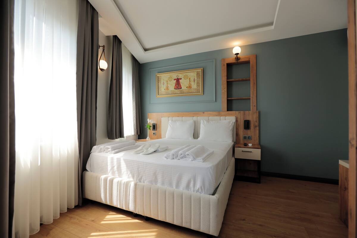 A neatly made bed with white linens and towels, a wooden headboard, a bedside table with a lamp, and a wall-mounted shelf.