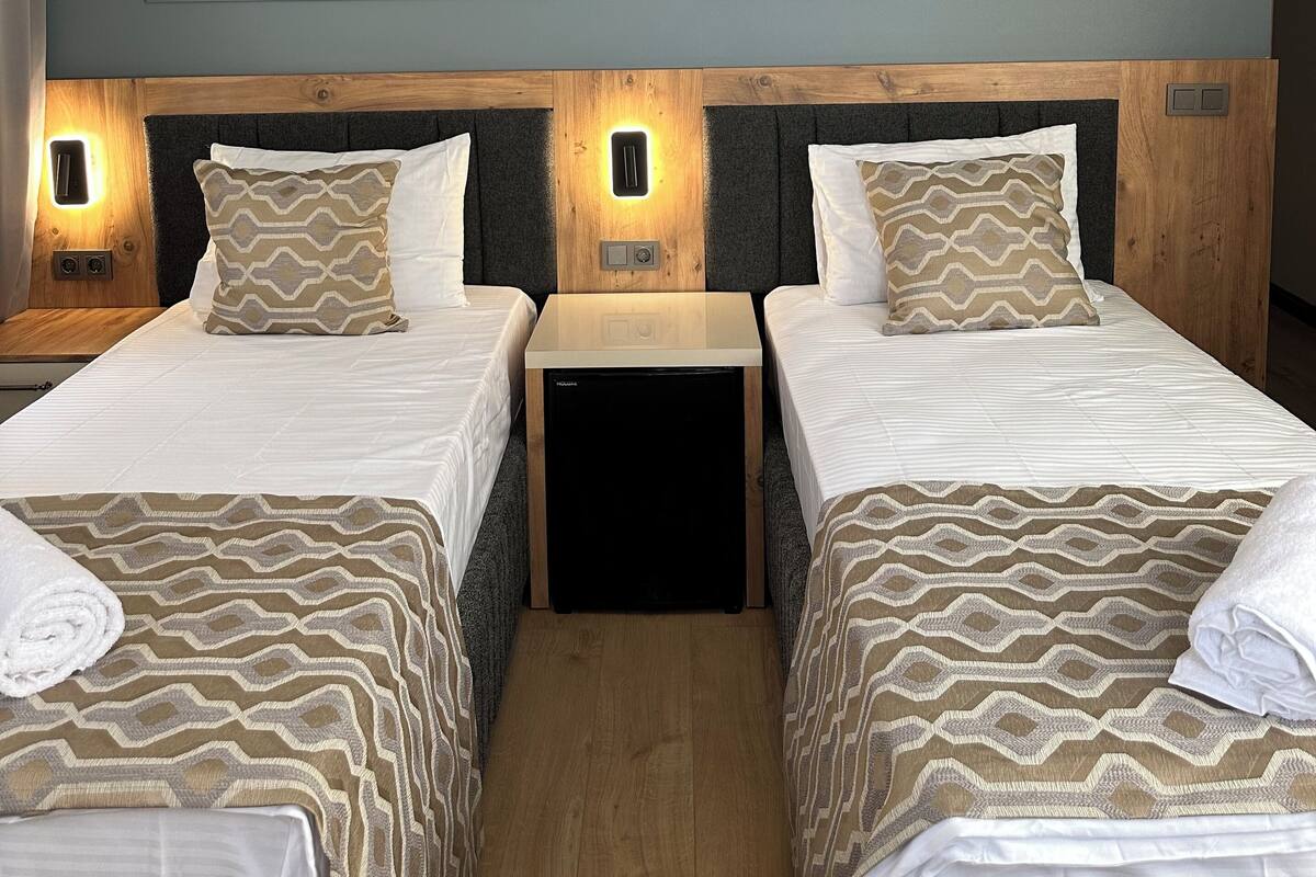 A hotel room with two beds, a wooden headboard, bedside lamps, and a small bedside table.