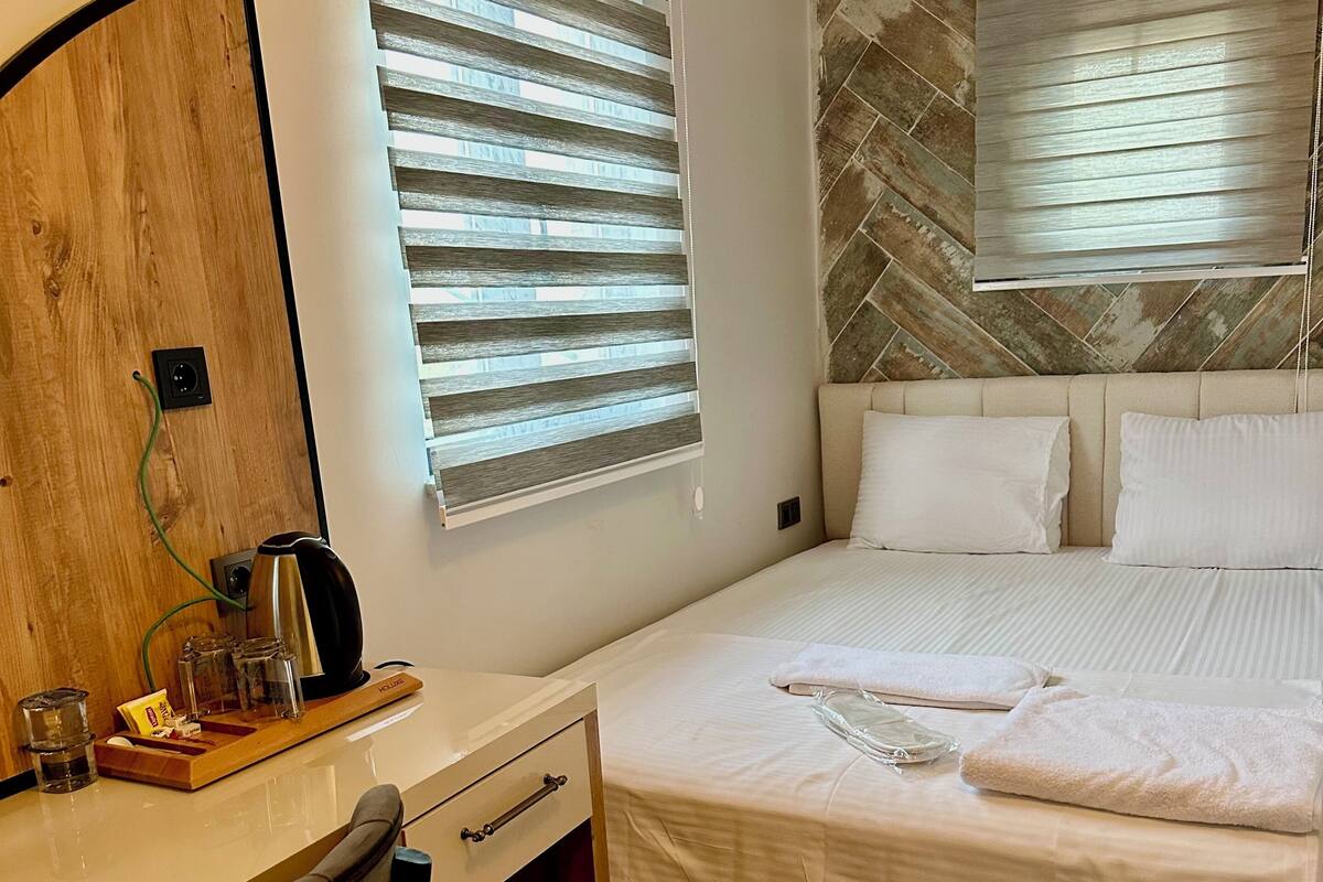 A hotel room with a wooden desk, a bed with white bedding, and a stone-patterned wall.