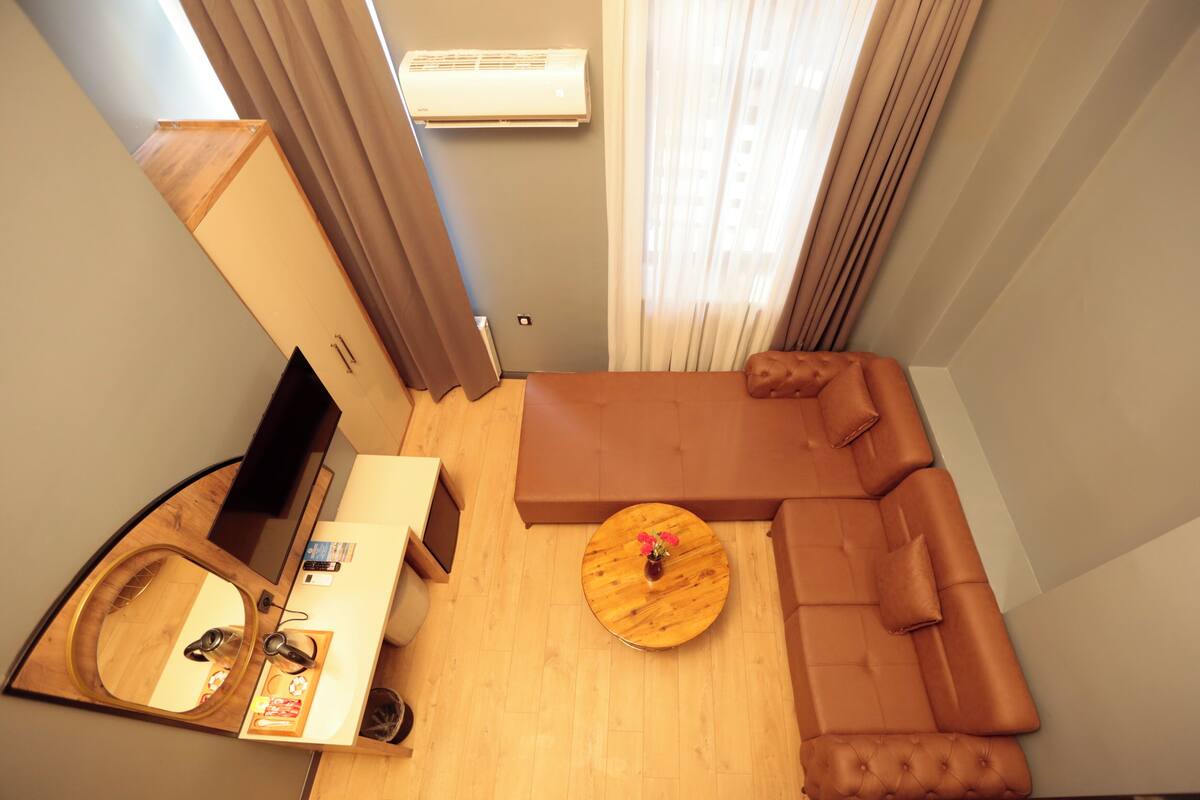 A compact living space with a sofa, a round wooden coffee table, a TV, and a small bathroom area.