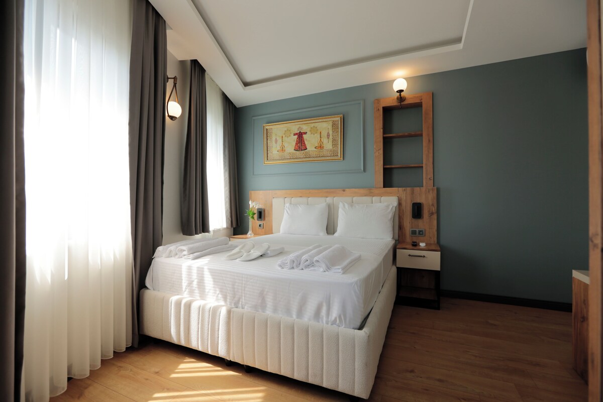 A neatly made bed with white linens and towels, a wooden headboard, a bedside table with a lamp, and a wall-mounted shelf.