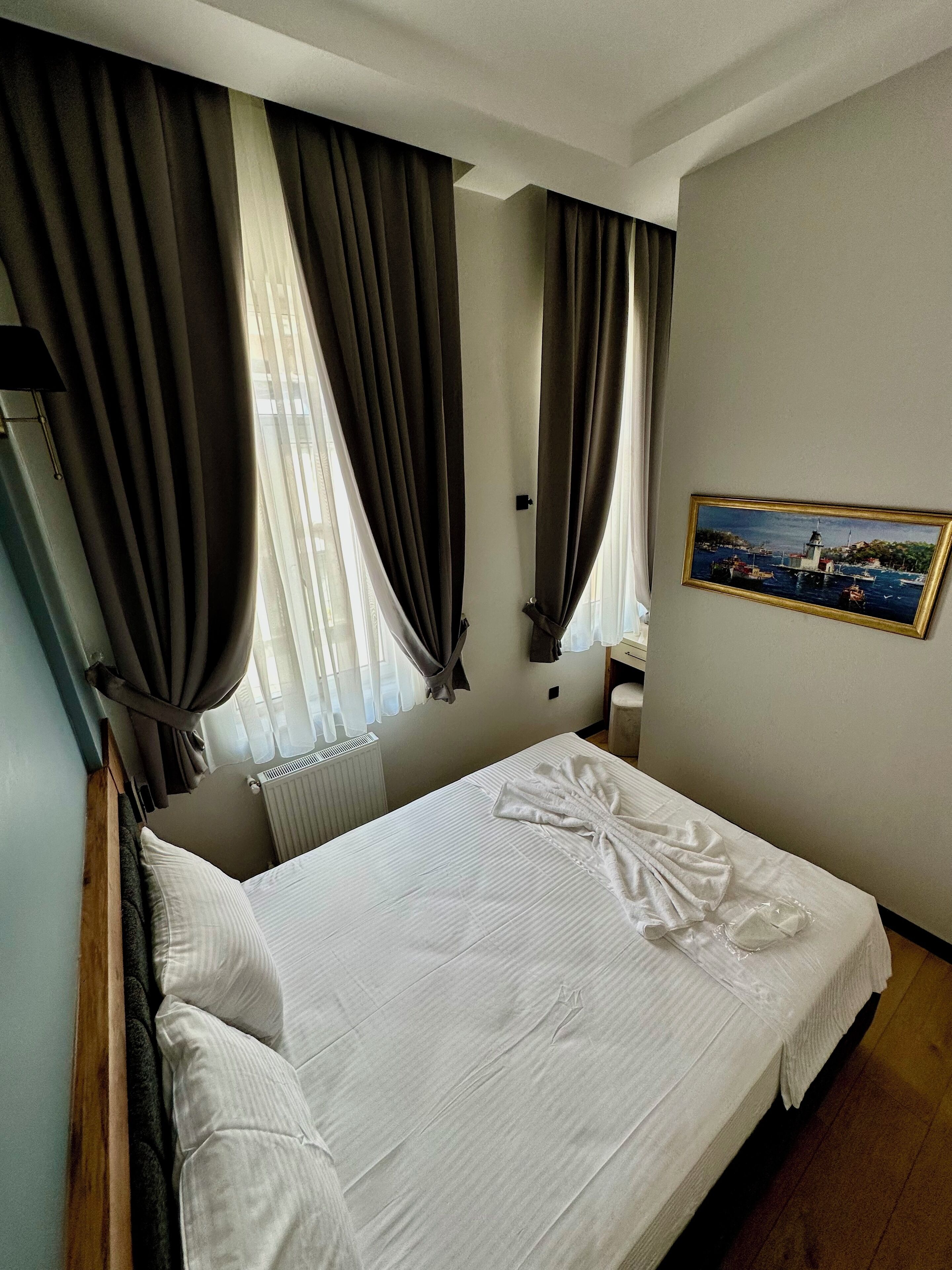 A hotel room with a neatly made bed, a framed picture on the wall, and a window with curtains.