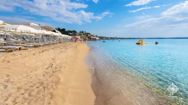 A beach with sun loungers and umbrellas, clear blue water, and a distant shoreline. - Villa Seaside - Dimora con jacuzzi a 200mt dal mare (Syracuse)