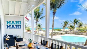 Een overdekte eethoek buiten met een houten tafel gedekt voor twee personen, met uitzicht op een zwembad en strand.