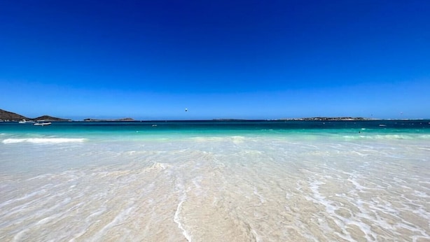 Een strand met helder turquoise water en wit zand.