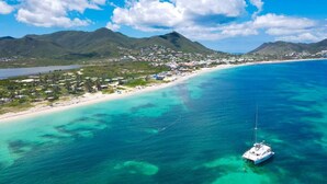 An aerial view of a coastal area with a clear blue sea, a beach, and a sailboat.