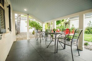 Eine überdachte Terrasse mit Tisch und Stühlen, umgeben von einem Garten und einem weißen Haus.
