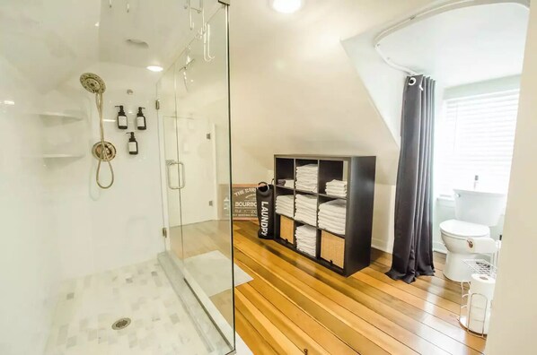 A modern bathroom with a glass shower enclosure, a wooden floor, a black storage unit with towels, and a white toilet.