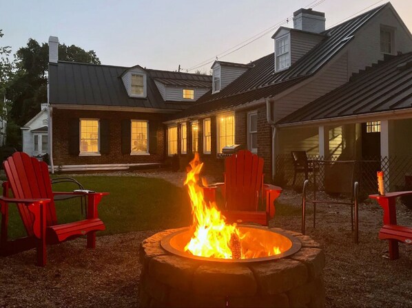 Ein Haus mit Feuerstelle im Garten, umgeben von roten Adirondack-Stühlen.