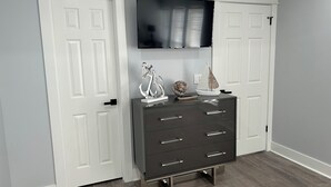 A room with a dark grey dresser, white doors, and a mounted TV on the wall.