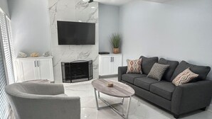A modern living room with a grey sofa, a grey armchair, a coffee table, a fireplace, and a TV mounted on the wall.