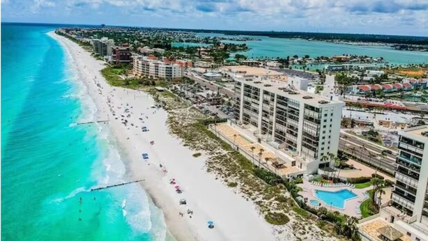 A coastal hotel with a beach view, multiple swimming pools, and a large building complex.