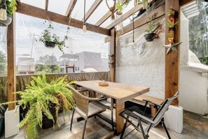 Relax in a serene patio area with a table and chairs, surrounded by lush plants and a large window offering a view of the surroundings.