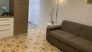 Ein Wohnzimmer mit einer Couch, einer Lampe, einem kleinen Tisch mit Pflanze und einer Tür zu einem Flur.