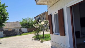 Ein gepflasterter Innenhof mit Hauseingang, ein kleiner Garten mit blühenden Pflanzen und ein Backsteinhaus im Hintergrund.
