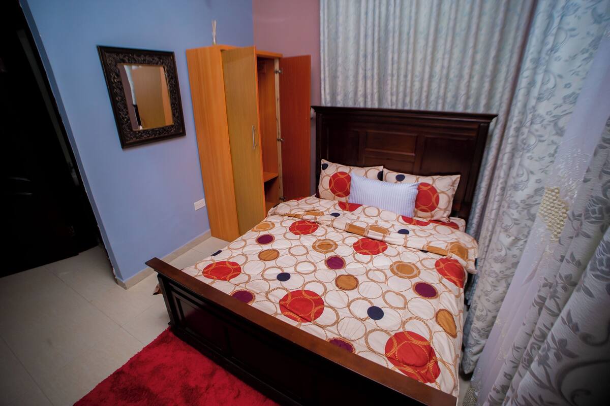 Ein Schlafzimmer mit einem hölzernen Bettgestell, einem roten Teppich, einem Kleiderschrank und einem Spiegel an der Wand.