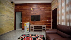 A living room with a brown leather sofa, a wooden entertainment unit, a flat-screen TV, and a patterned rug. - Bays Villa (Koforidua)