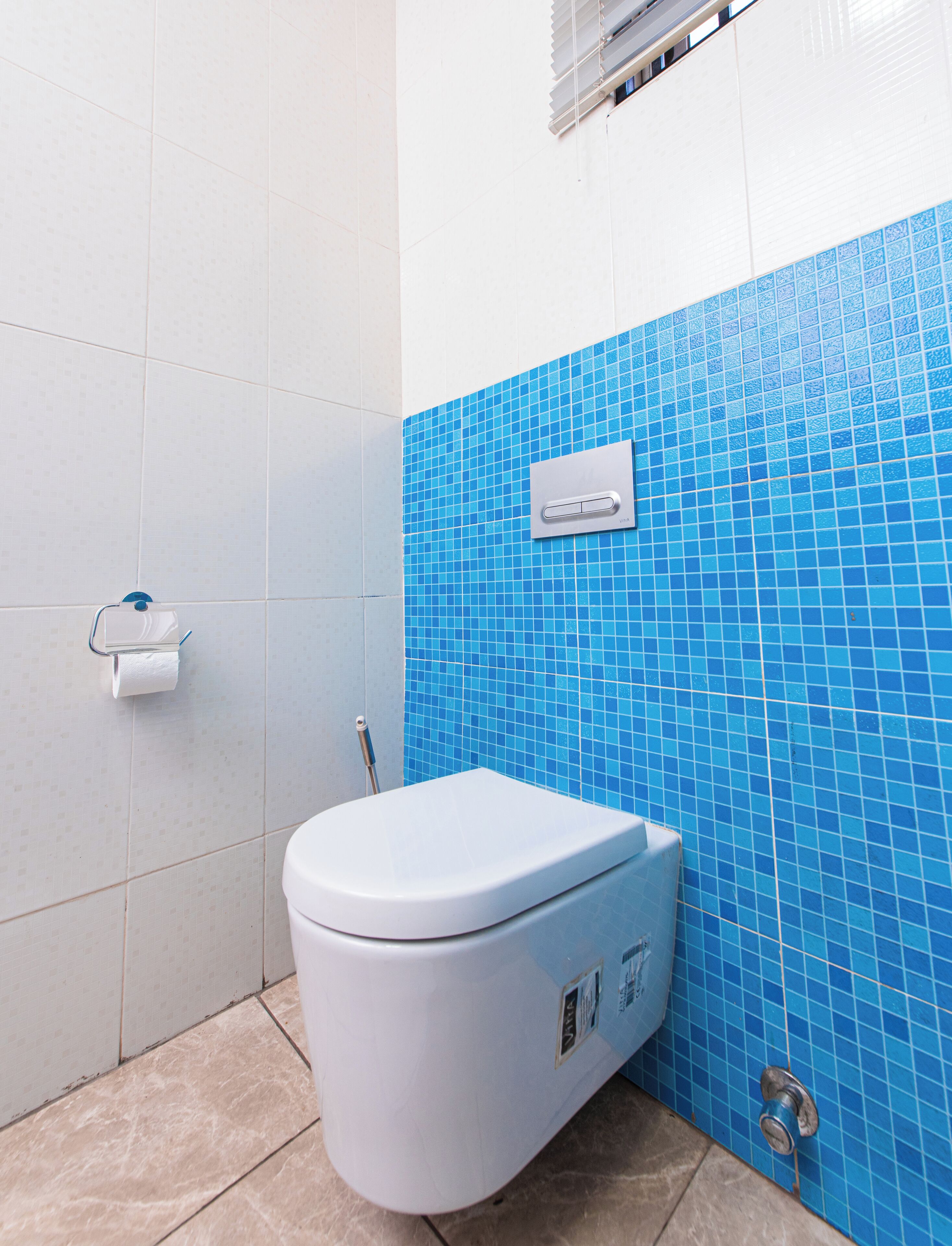 A bathroom with a white toilet, a blue-tiled wall, and a hand dryer.