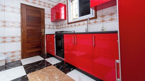 A kitchen with red cabinets, a black stove, and a checkered floor. - Bays Villa (Koforidua)