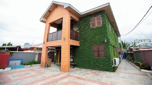 A two-story house with a balcony, a covered porch, and a green ivy-covered wall. - Bays Villa (Koforidua)