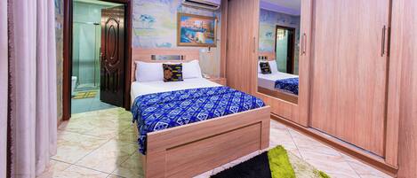 Une chambre à coucher comprenant un lit, une armoire, un miroir et une porte donnant sur une salle de bain.