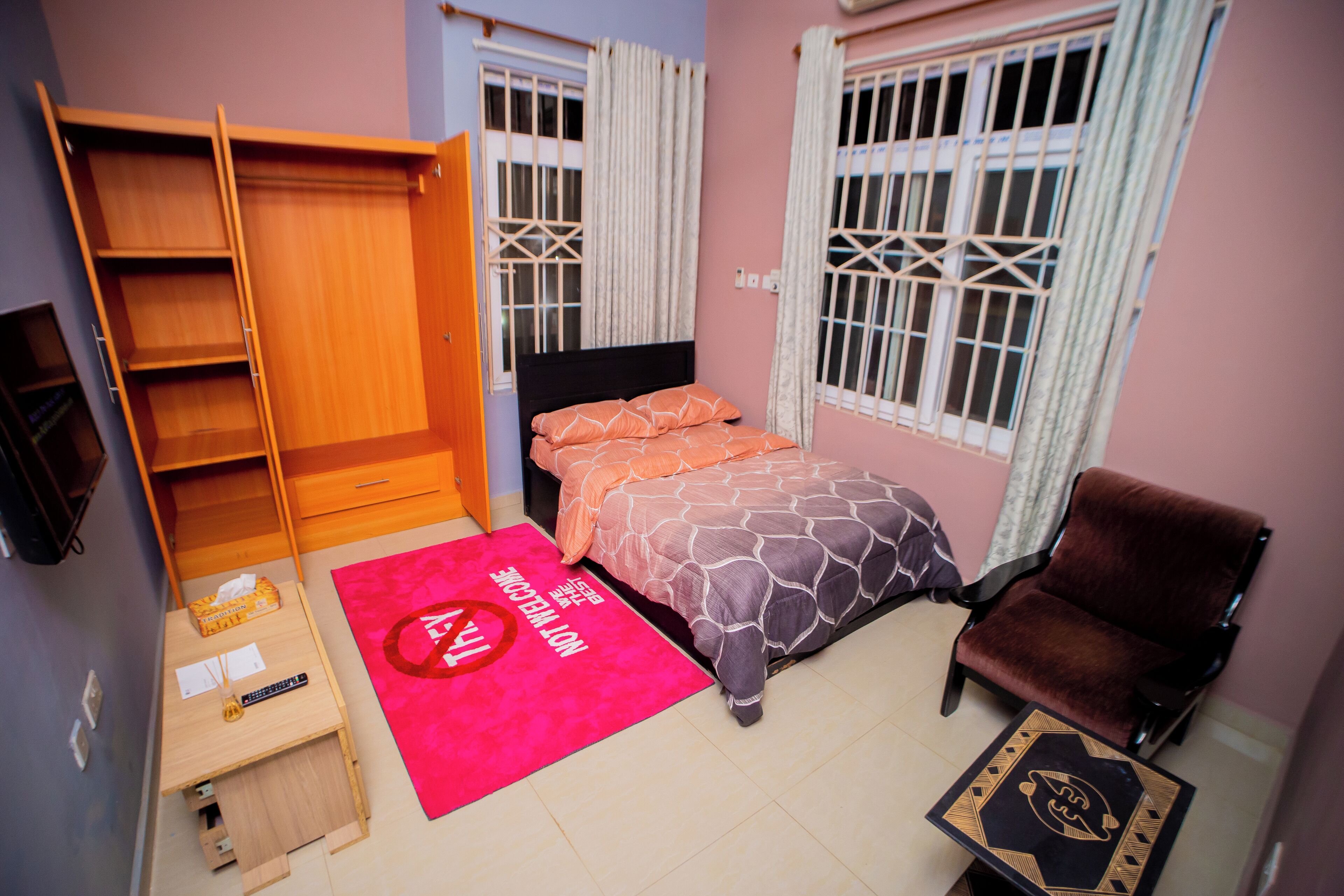 A bedroom with a bed, a wardrobe, a chair, a small table, and a window with curtains.