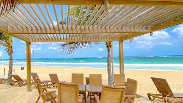 Eine hölzerne Strandkabine mit Tisch und Stühlen mit Blick auf Strand und Meer.